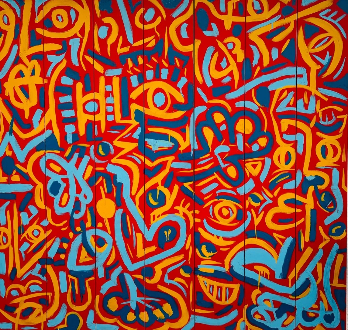 Trazos gruesos de amarillo y celeste que forman ojos y rostros, sobre un fondo rojo de tablas verticales. Sin título. Esmalte sobre hierro, 200 x 200 cm, 2024. Caracas. Nicolás Lapadula