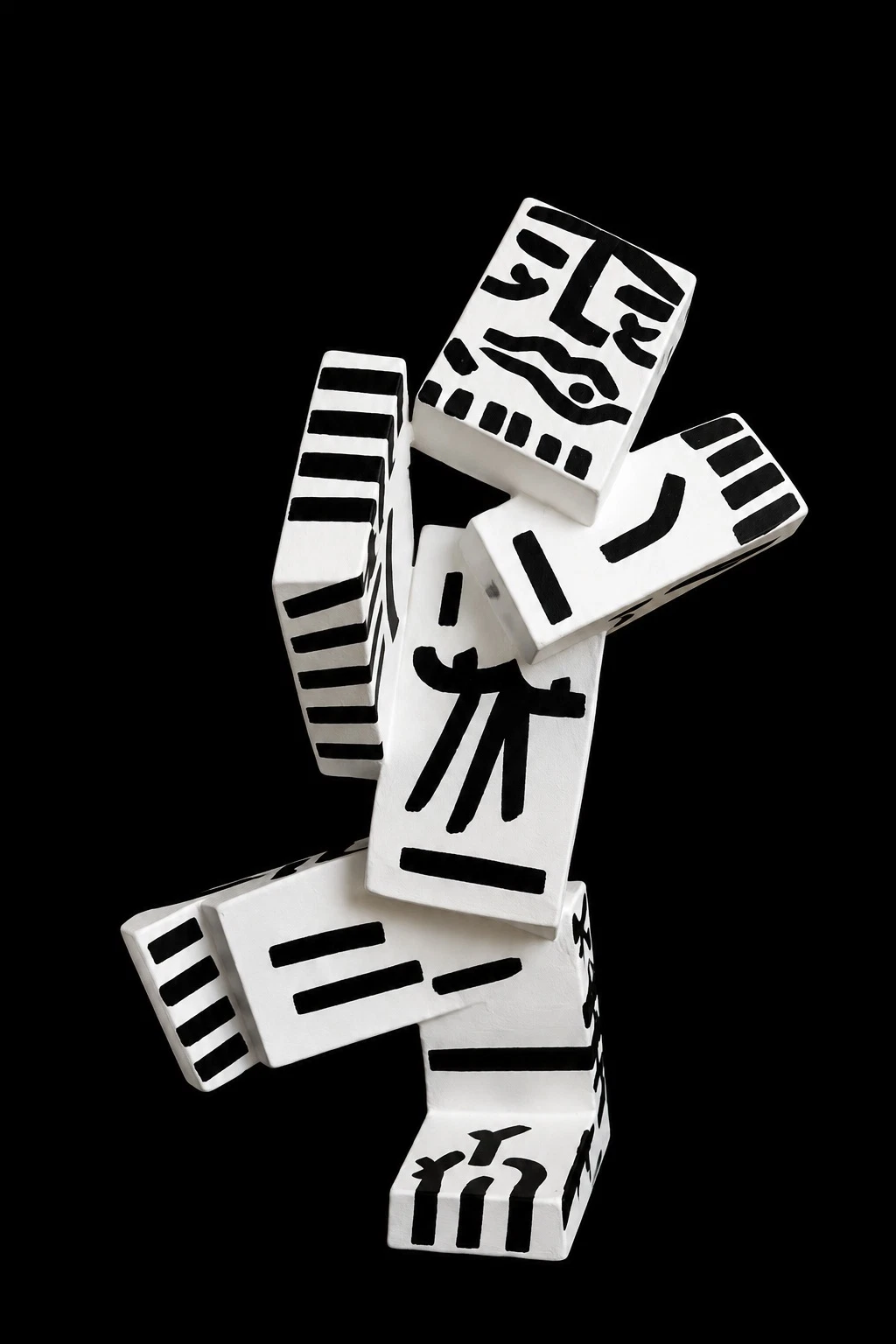 Escultura de bloques blancos apilados en forma de figura humana, con rasgos y líneas pintados en negro sobre fondo negro. Sin título. Nicolás Lapadula