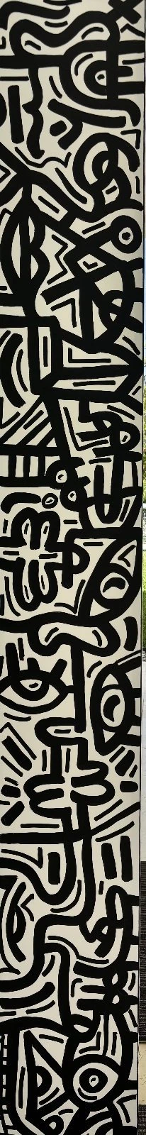 Pila vertical de rostros y figuras en trazo negro denso sobre fondo blanco, en una tira muy estrecha. Sin título. Acrílico sobre lienzo, 240 x 30 cm, 2026. Caracas. Nicolás Lapadula