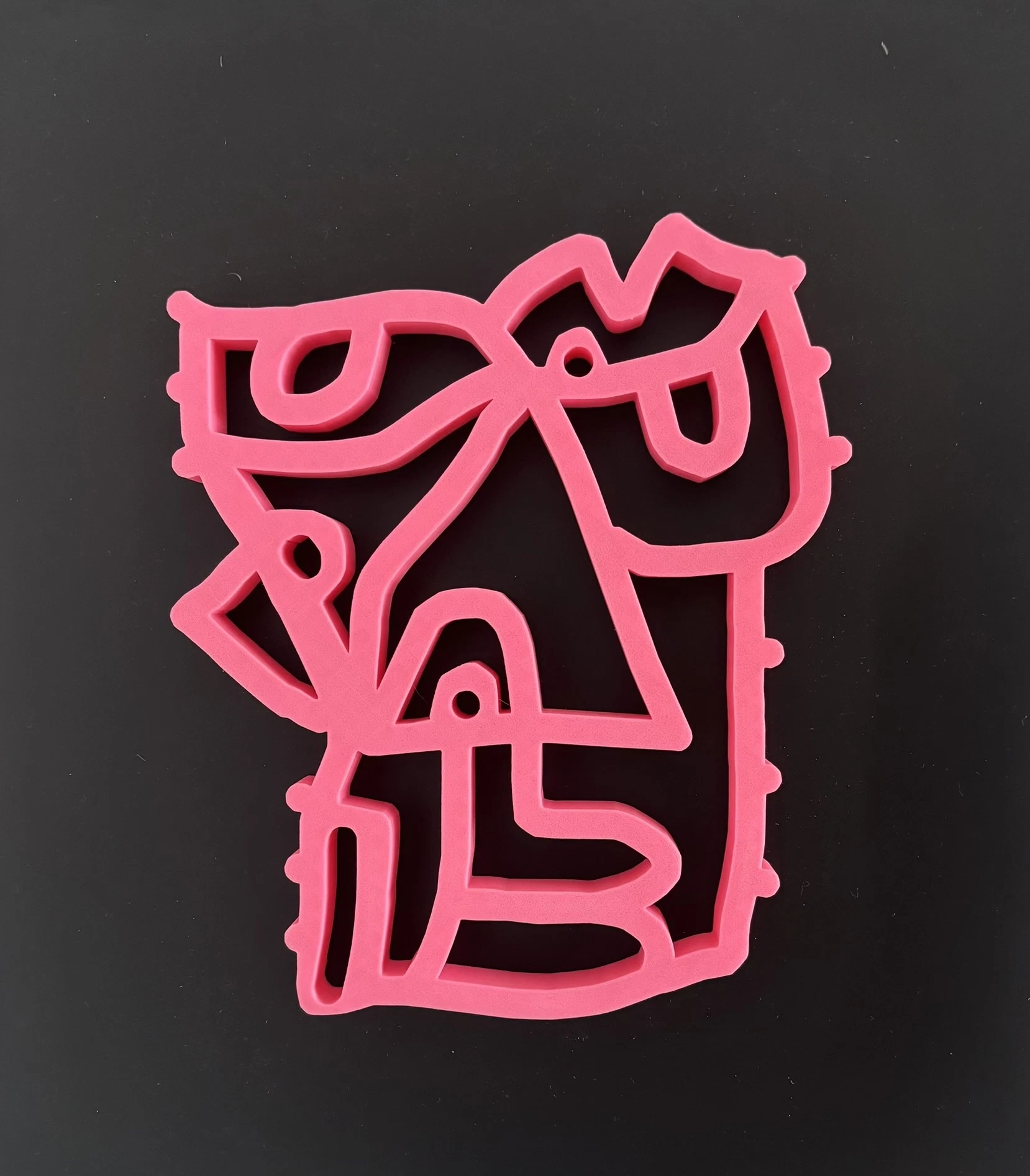 Rostro de trazo continuo en relieve de color rosa intenso, con perforaciones pequeñas y puntos en el borde, sobre un fondo negro liso. Sin título. Impresión 3D sobre acrílico, 35 x 40 cm, 2026. Caracas. Nicolás Lapadula
