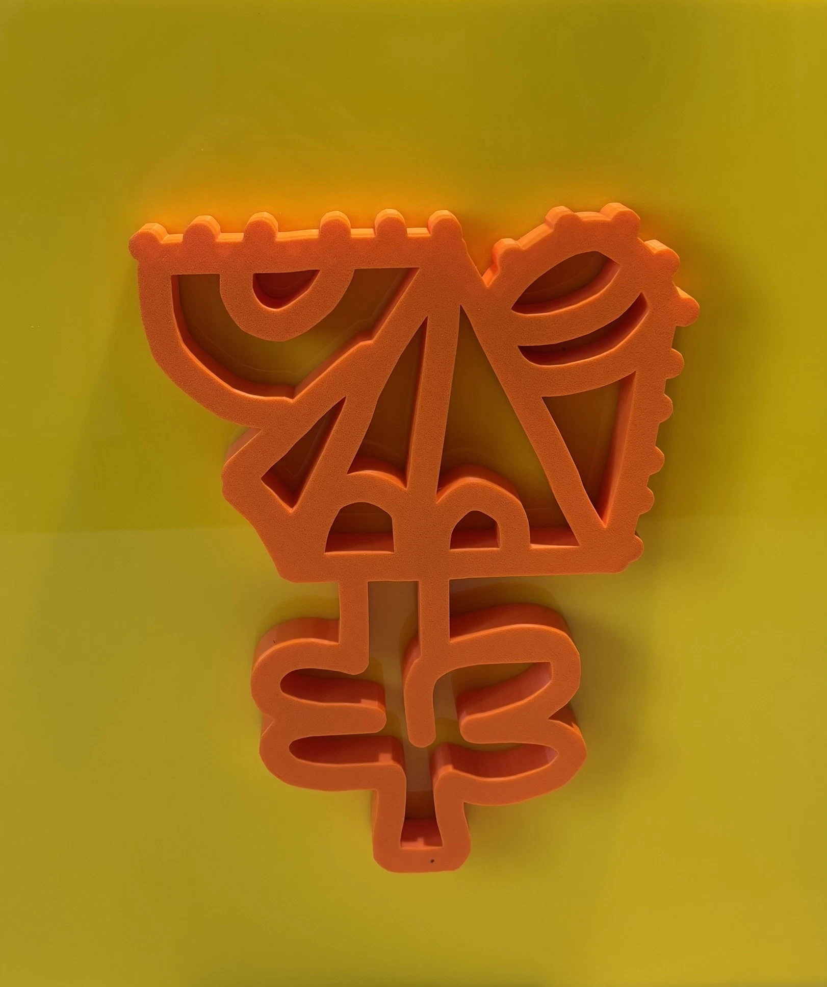 Rostro de trazo continuo en relieve naranja con una forma de hojas en la base, sobre una placa de acrílico amarilla. Sin título. Impresión 3D sobre acrílico, 35 x 40 cm, 2026. Caracas. Nicolás Lapadula