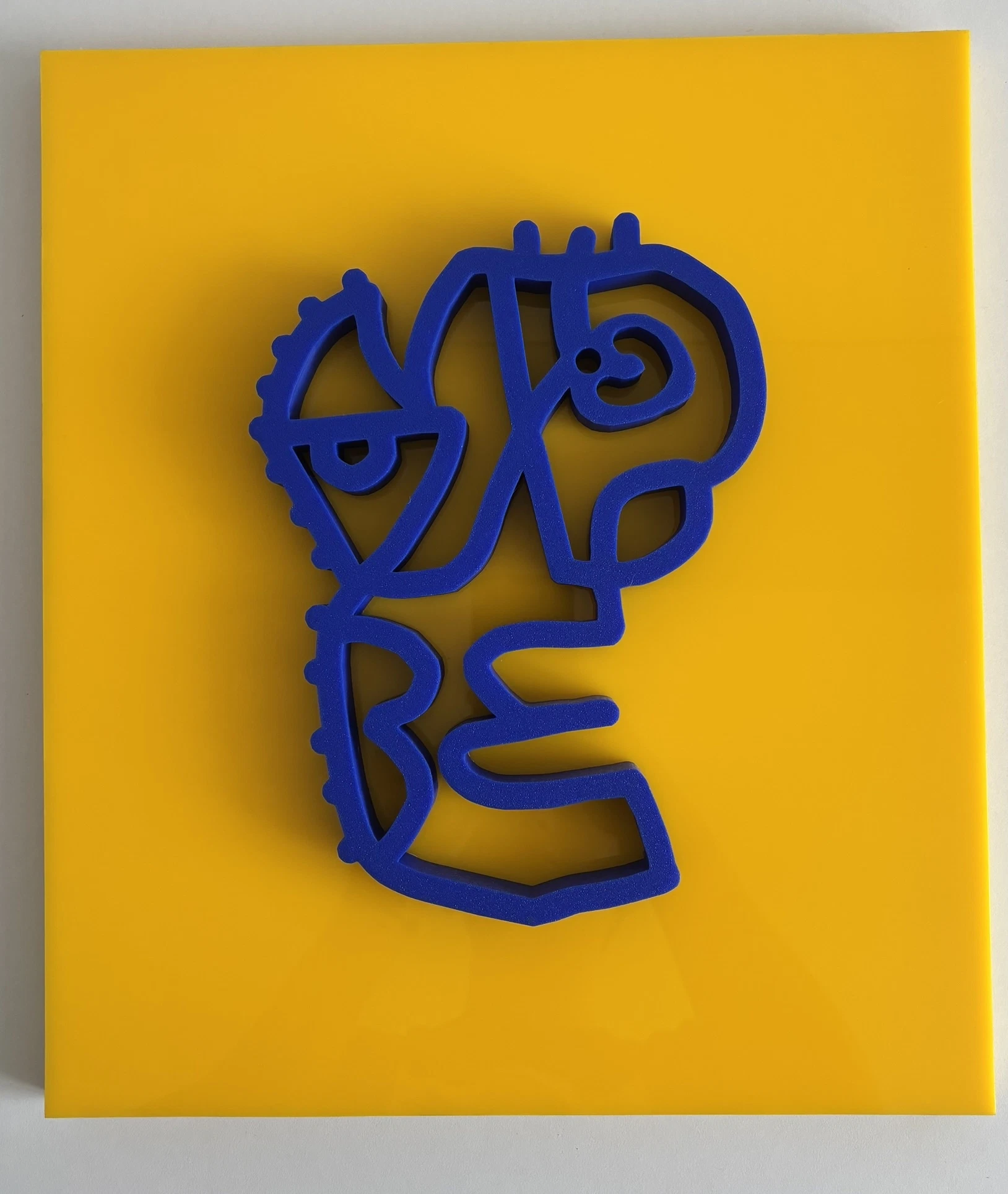 Rostro de trazo continuo impreso en 3D, de color azul eléctrico, sobre una placa de acrílico amarilla. Sin título. Impresión 3D sobre acrílico, 35 x 40 cm, 2026. Caracas. Nicolás Lapadula