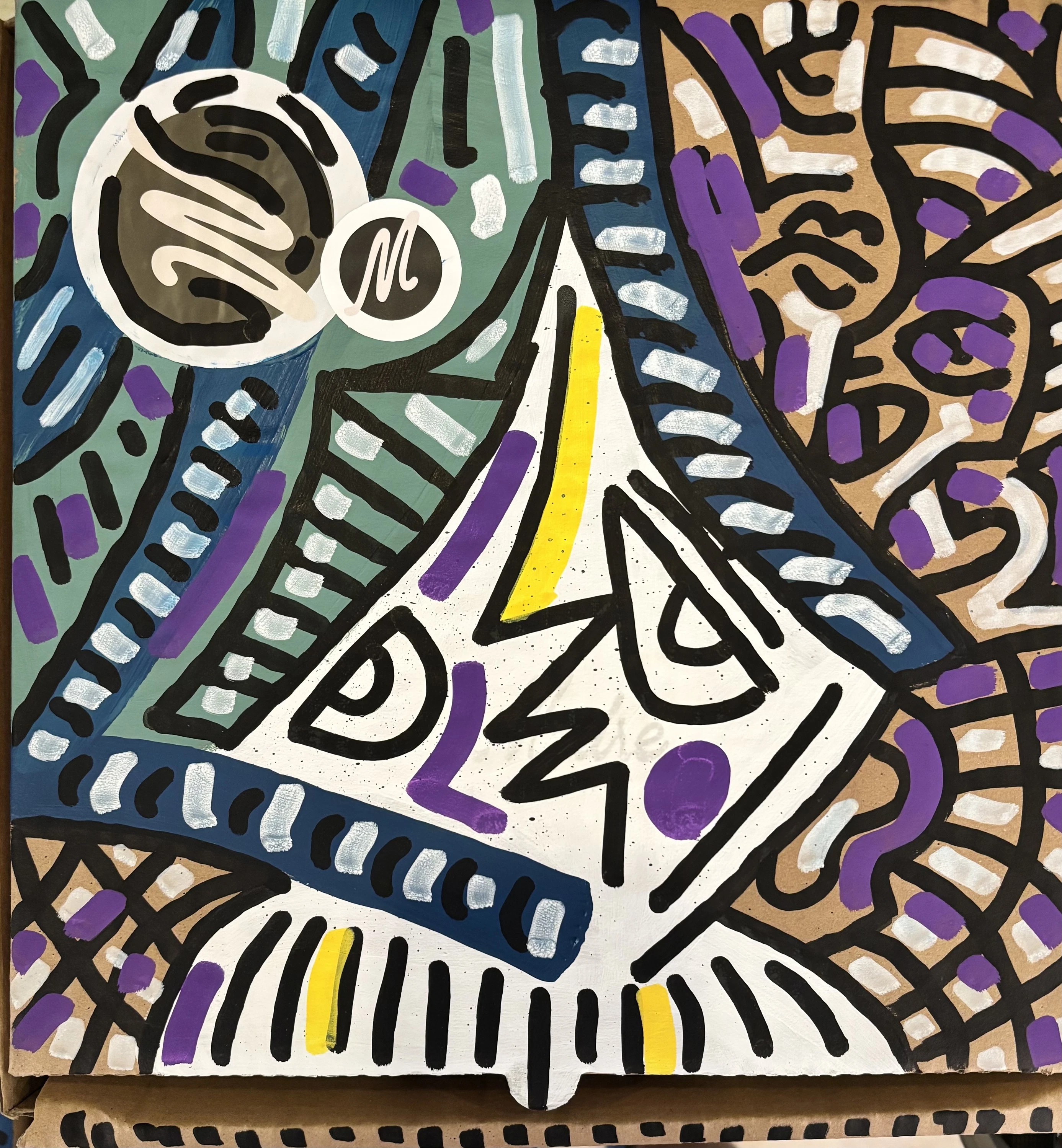 Rostro triangular blanco con una barra amarilla, rodeado de líneas negras, azules, violetas y celestes pintadas sobre una caja de cartón. Sin título. Acrílico sobre cartón, 40 x 40 cm, 2026. Caracas. Nicolás Lapadula
